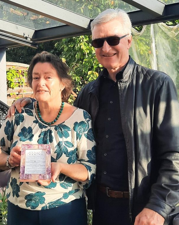 Eine Frau mit Blumenbluse hält einen Preis, neben ihr steht ein Mann in Sonnenbrille.