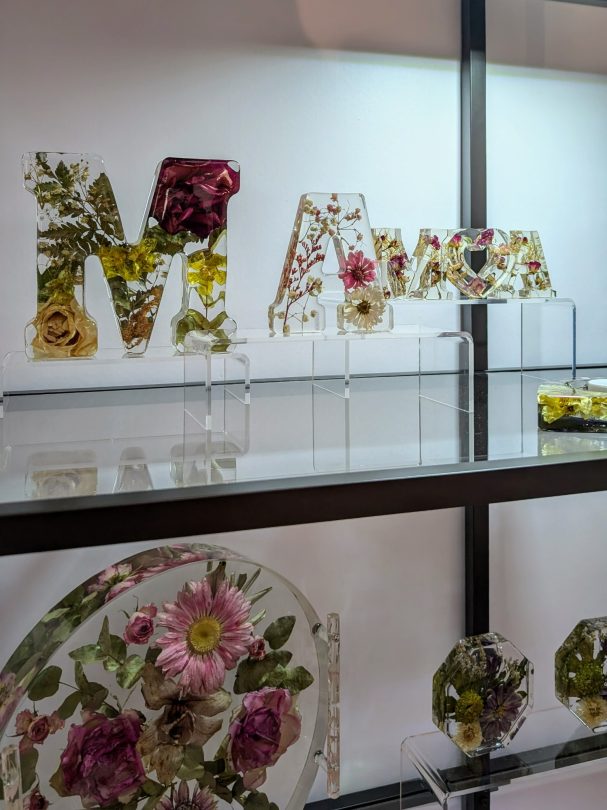 Bunte Buchstaben aus getrockneten Blumen, auf einem Regal ausgestellt.