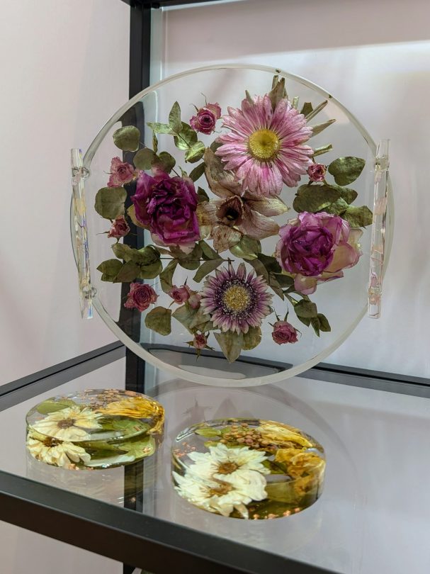 Runde Acrylplatte mit gepressten Blumen in Rosa- und Lilatönen, darunter zwei kleine Platten.