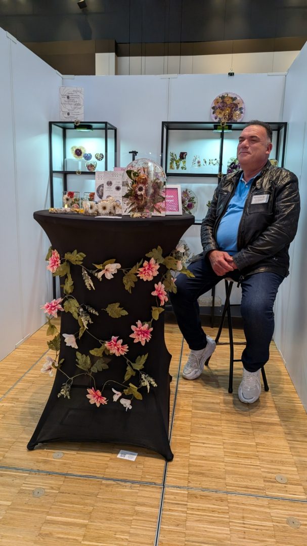 Mann sitzt auf einem Stuhl neben einem Tisch mit Blumenornamenten.