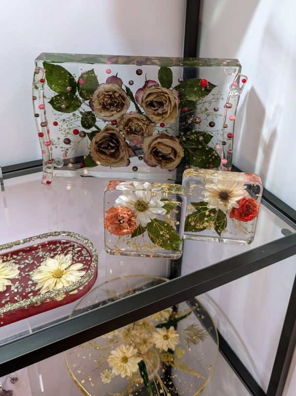 Farbige, eingegossene Blumenarrangements in transparentem Kunstharz auf einem Regal.